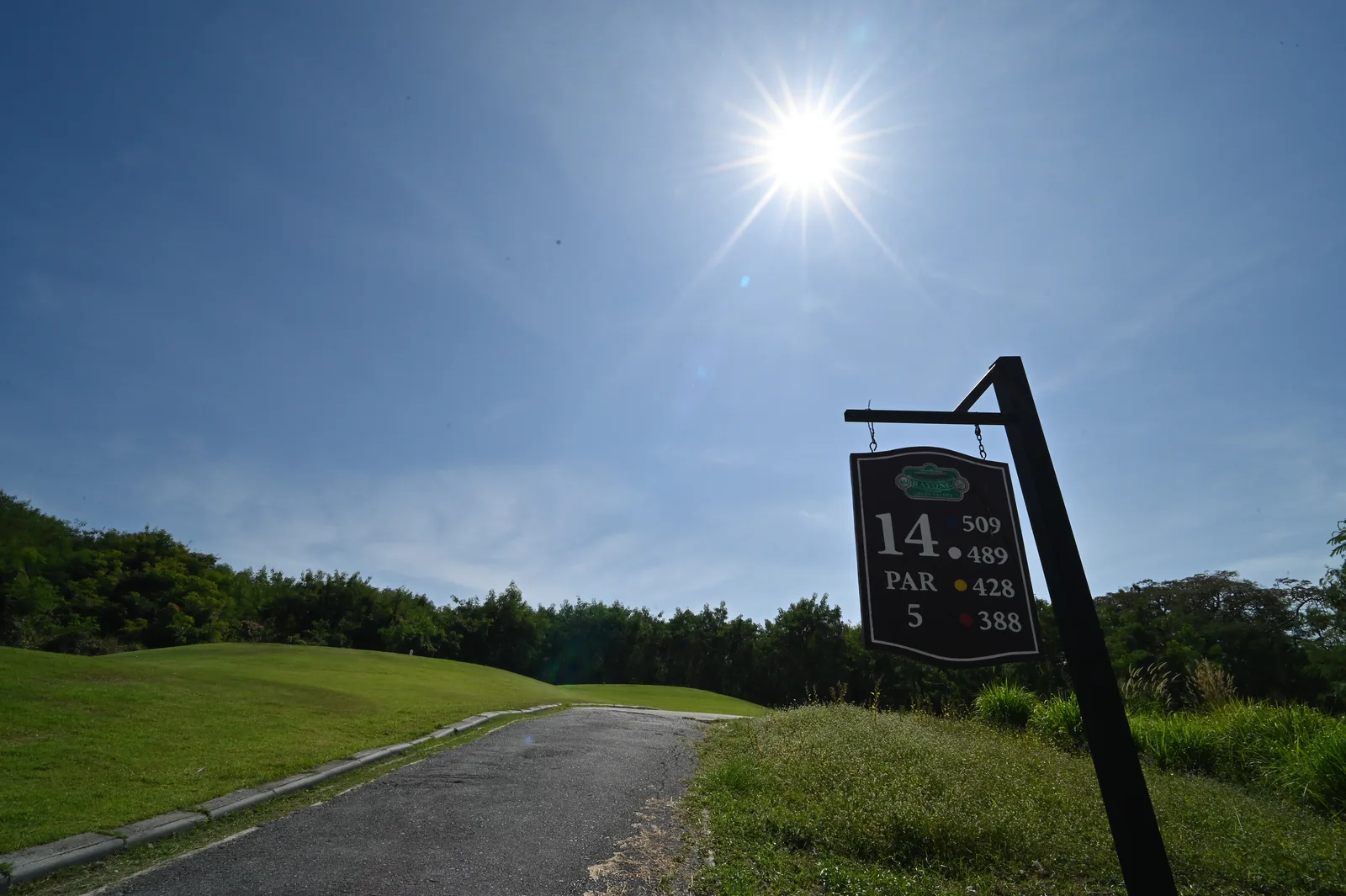 A Rayong Green Valley sign for Hole 14, par 5, beside a cart path and tee area under a bright sun in December 2025.